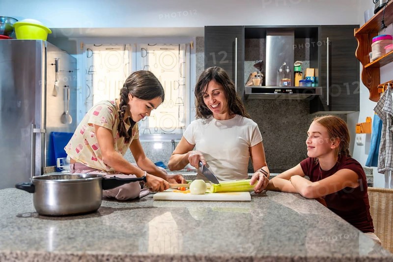 Mother and daughters happily preparing food in a home kitchen, chopping ingredients for healthy meal, fostering connection and domestic activity during a daily family session