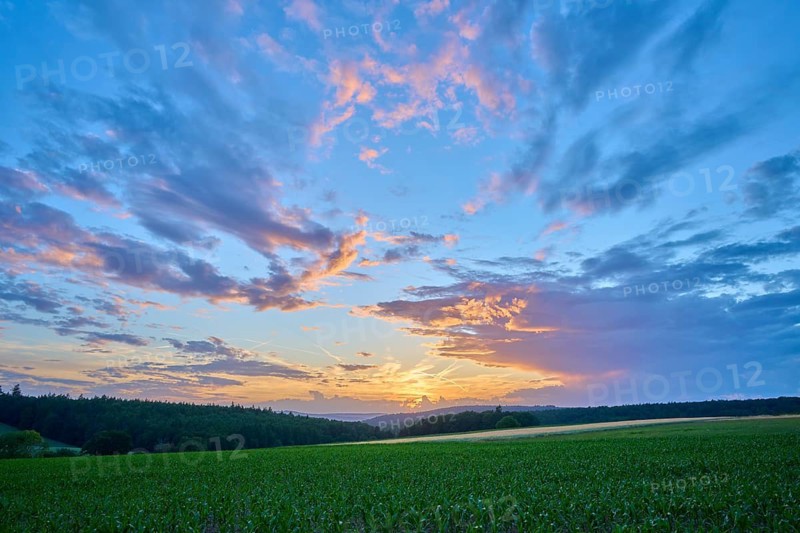 Sunset over a green field with dramatic clouds and intense sky, summer, Großheubach, Miltenberg, Spessart, Bavaria, Germany