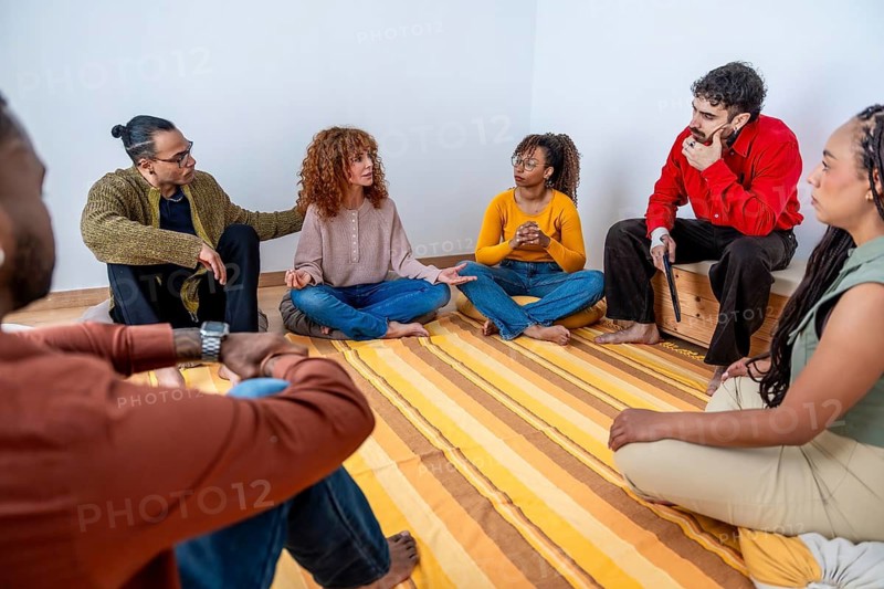 Diverse adults seated in a circle indoors, sharing stories and actively listening in a supportive group therapy session that fosters empathy, trust, healing and mental wellness