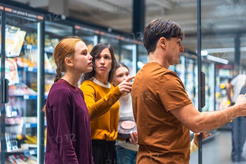 Family comparing products and making decisions together in the frozen food aisle of a supermarket, selecting items for their weekly shopping list while browsing options