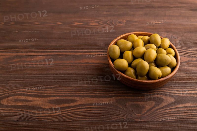 Fresh green olives in wooden bowl on brown wooden background. side view, copy space