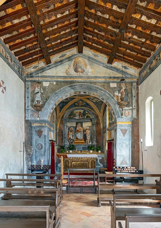 Historic interior of San Rocco Church with religious frescoes, stone arch, altar, wooden pews, and open timber roof, Limone Sul Garda, Italy