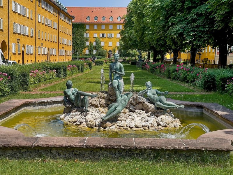 Yellow residential buildings, courtyard, bronze figures on rocks in the well, borstei, heritage-protected housing estate, Munich, Bavaria, Germany