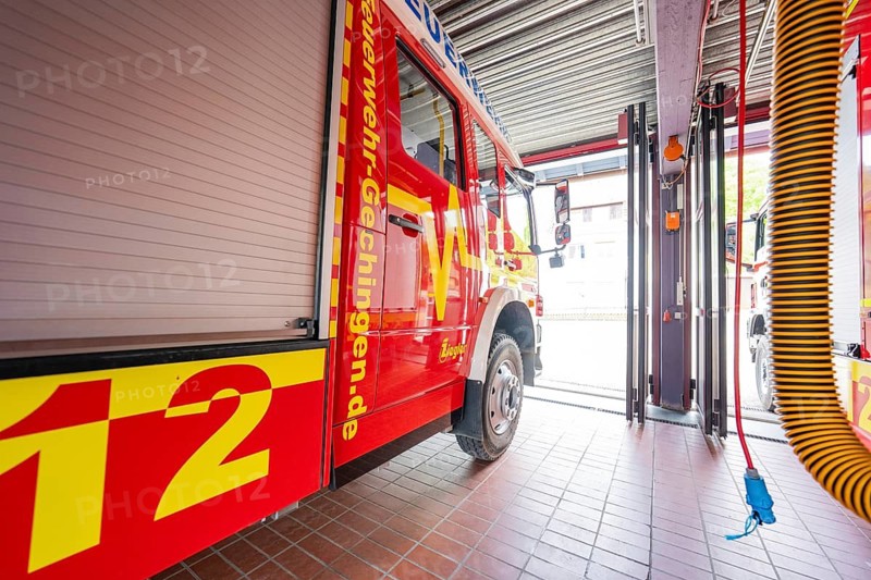 Red fire engine in a large garage room with visible hose on the ceiling, Gechingen fire department, Calw district, Germany