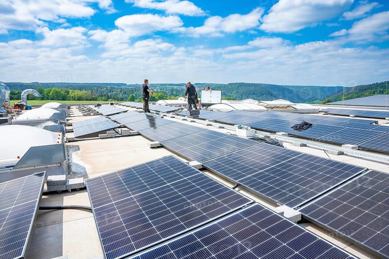 Two workers look after solar cells on a large roof under a blue sky, PV Montage, Perrot, Calw, Germany