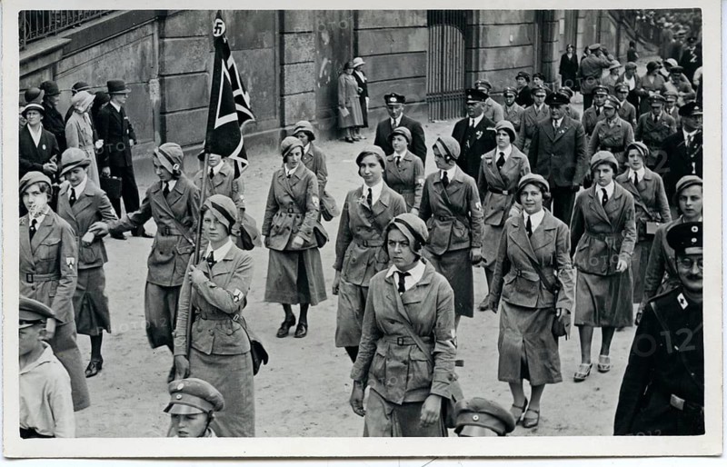 Women in uniform, BDM, patriotic flag, National Socialism, organization, march, rally, lift, caps, marching in an urban environment, some wearing caps, black and white photography, Julius Gross, around 1933