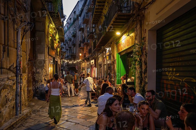 Busy narrow street with mostly young people dining outside restaurants, atmospheric lighting, Palermo, Sicily, Italy