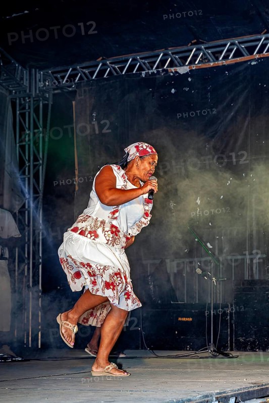 Woman dancing singing on a smoking stage in a floral dress, a band playing and dancing at a festival in Petrolina in Brazil