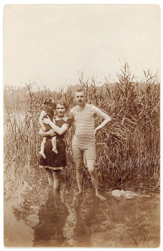 Bathing, swimwear, woman, men, children, leisure, fun, summer, A couple with a child standing on the shore in shallow water next to thick reeds, around 1920