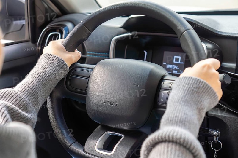 Detail of student driver's hands gripping steering wheel, digital speedometer showing zero, airbag label, car interior, learning to drive concept