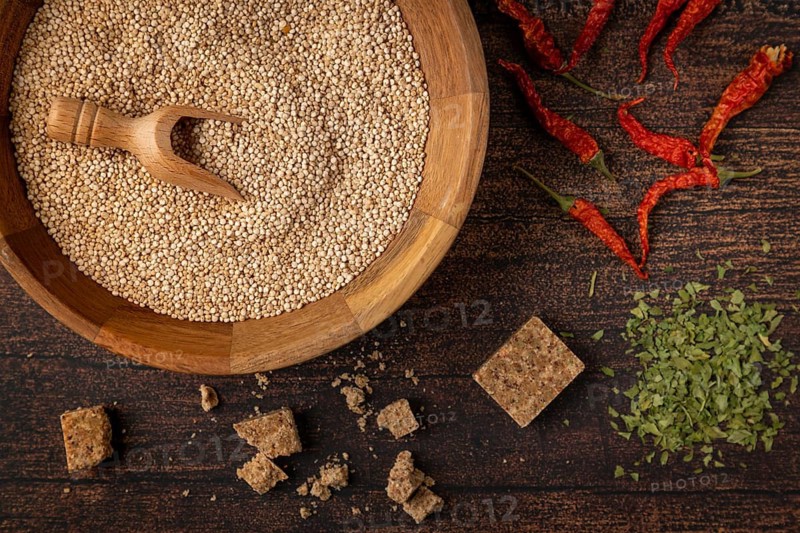 A bowl filled with quinoa next to spices and dried red peppers on a wooden table
