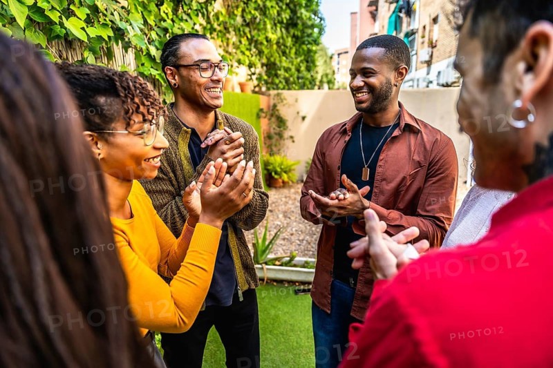Diverse friends clapping and smiling in an outdoor group therapy circle, sharing support, empathy and connection in a sunny backyard wellness session for mental health