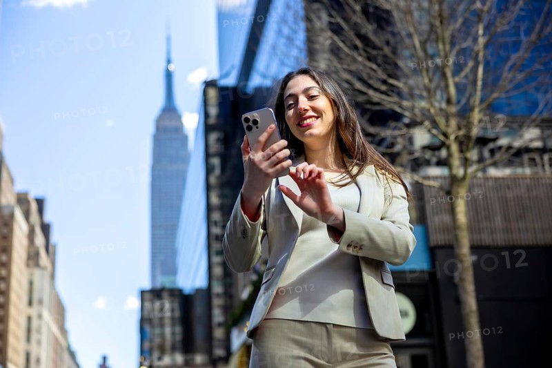 Young businesswoman smiling and interacting with her phone while walking in manhattan, symbolizing urban connectivity, communication, and managing work life balance on the go