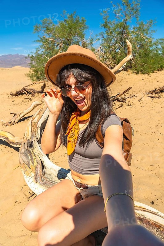 Adventure traveler woman exploring dry arid mesquite flat sand dunes in death valley national park, taking a selfie and sharing her exciting outdoor journey