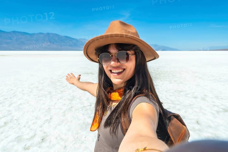 Young woman traveler smiling and extending arm, capturing a vibrant selfie on the vast salt flats of badwater basin in death valley national park under a clear blue sky