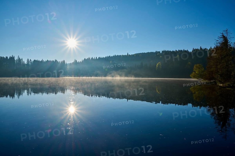 The sun rises over a still lake with light fog on the water surface, Windgfällweiher, Lenzkirch, Black Forest, Breisgau Hochschwarzwald, Baden-Württemberg, Germany