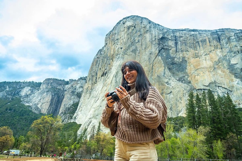 Smiling woman photographing el capitan and the sweeping yosemite valley vista on a sunny hike, enjoying nature, adventure and the iconic granite cliffs in california wilderness