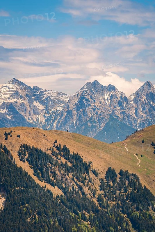 Snowy mountain peaks with forests and a winding hiking trail in hilly surroundings, Hahnenkamm, Kitzbühel, Austria
