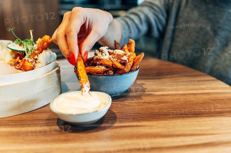 Woman dipping sweet potato fries into creamy sauce at a cozy restaurant