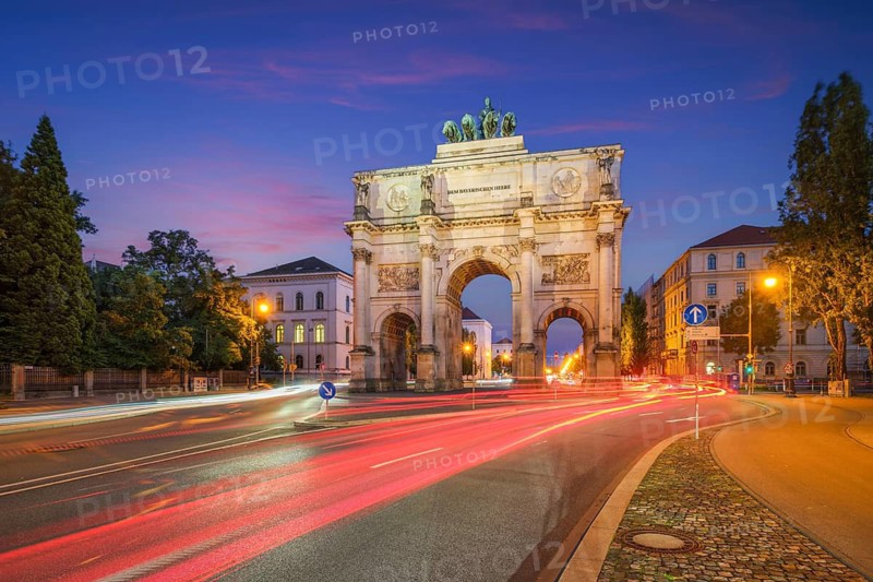 Long exposure of the illuminated Siegestor in Munich, Bavaria, Germany, featuring colorful red and white traffic light trails at blue hour