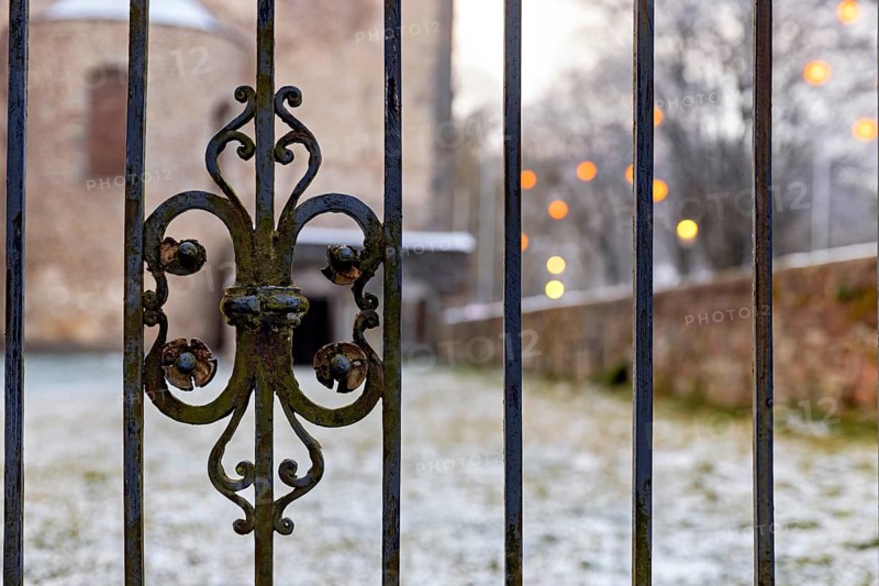 Decorated iron fence in the foreground with a brick building and illuminated lights in the background on a snowy winter day, iron bars at the abbey ruins in Bad Hersfeld