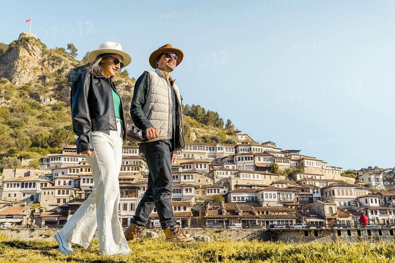 Happy travel couple walking historic Berat hillside town Albania traditional Ottoman houses sunny autumn vacation sightseeing