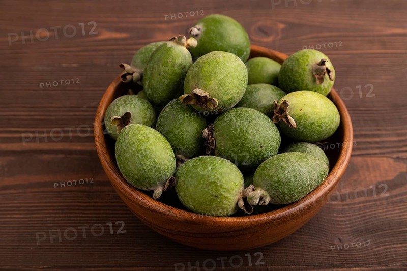 Ripe Feijoa in wooden bowl on brown wooden background, side view, close up, minimalism