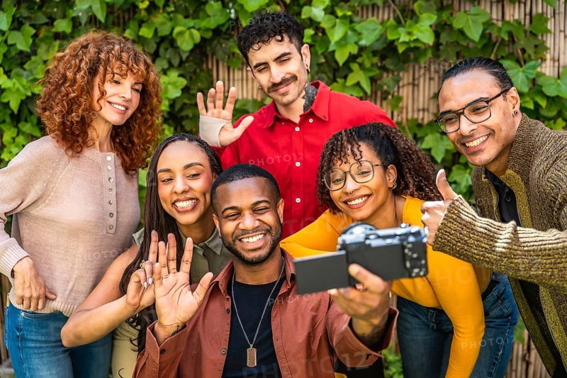 Diverse group of smiling friends recording a video, showing connection, community, and support while documenting happy moments and shared experiences in an outdoor setting