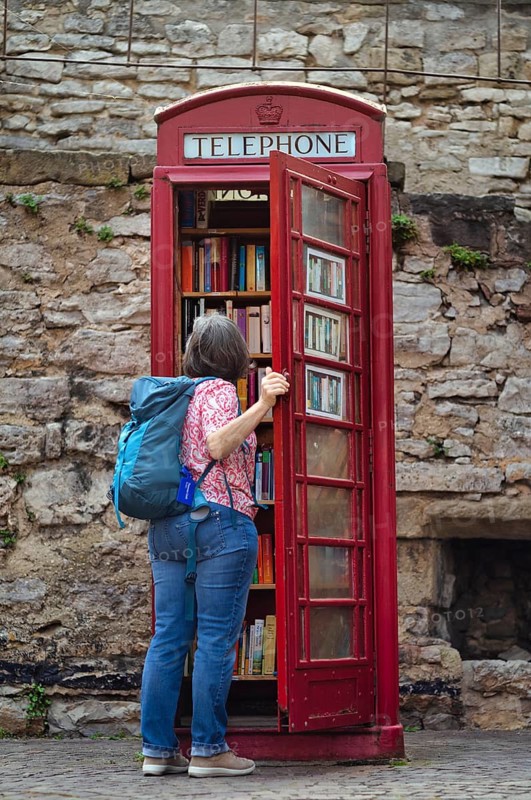 Elderly woman looks at old red English telephone box, telephone, serves as library, public bookcase, old town, Besigheim an der Enz, Baden-Württemberg, Germany