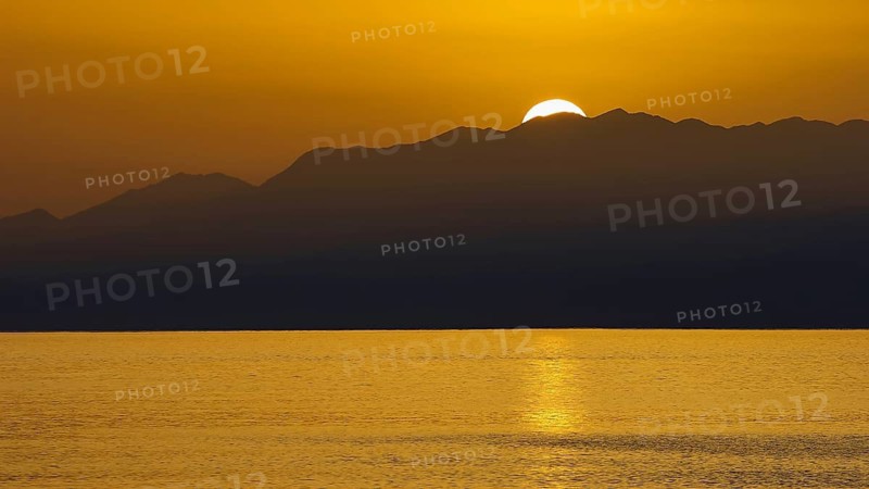 Sunset over mountains with golden light reflecting in calm sea, Matala, South Coast, Crete, Greek Islands, Greece