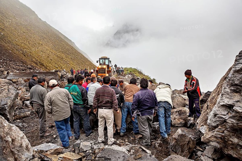 People work together to move a rock on a foggy mountain road with a tractor, rockslide on the pass road towards Rurrenabaque through the Andes on the Road of Death in Bolivia