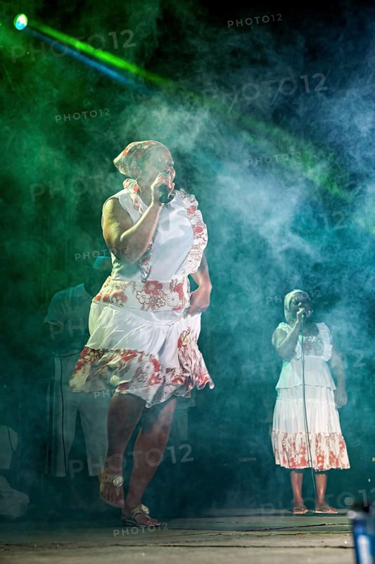 Singer in an intense stage atmosphere with microphone and fog effects, a band plays and dances at a festival in Petrolina in Brazil