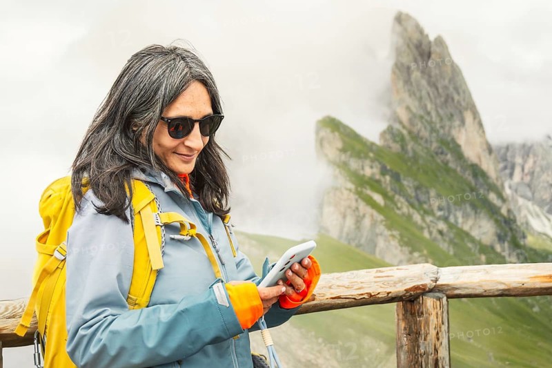 Smiling woman hiker checking mobile GPS navigation app type message, use social media on smartphone using satellite connectivity or esim in Seceda mountain ridge walk. Dolomites Italy holidays