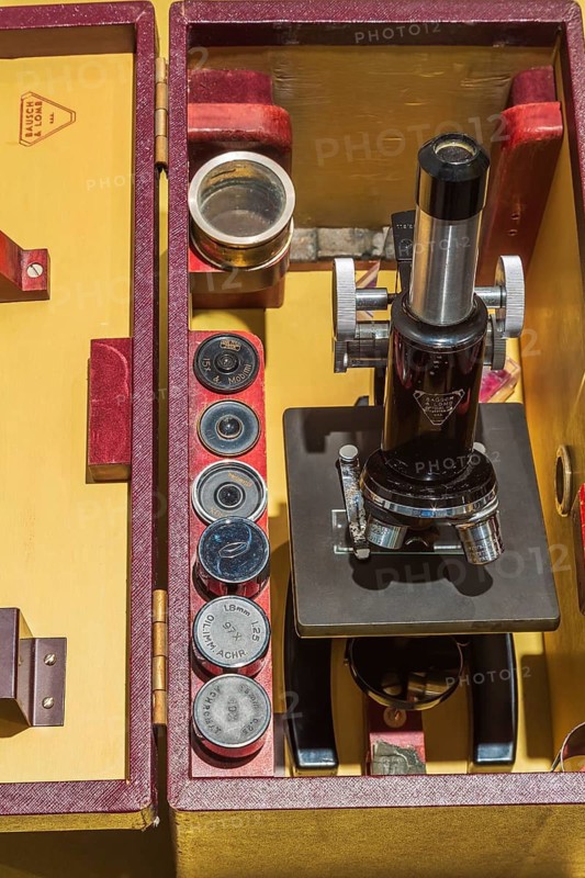 Stored vintage black Bausch & Lomb research microscope with objective lenses in opened brownish red synthetic leather and wood carrying case, Studio Composition, Quebec, Canada