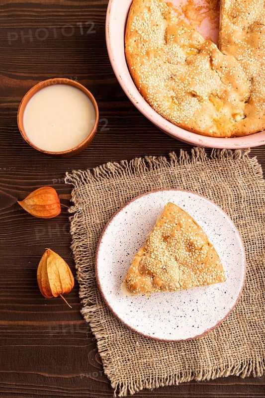 Apple Charlotte cake on brown wooden background and linen textile, cup of milk, top view, flat lay, close up