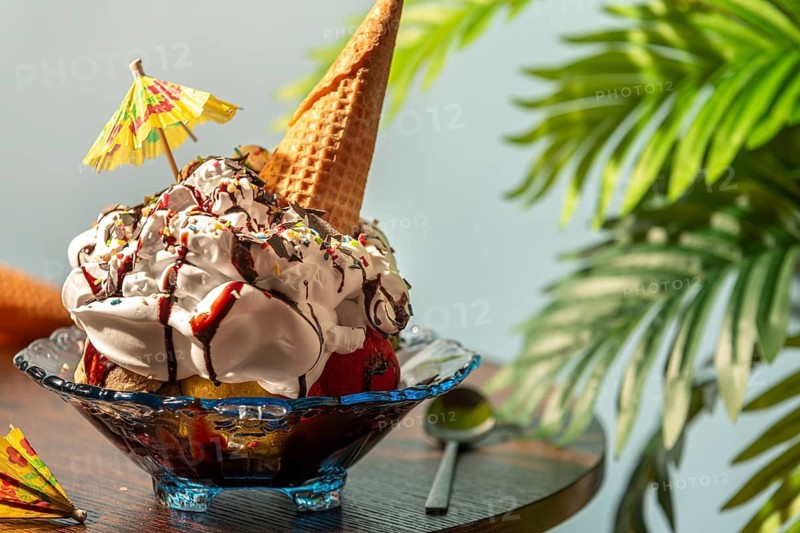 A decorated ice cream sundae with cream, umbrella and waffle on a table