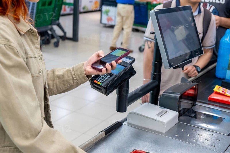 Woman using a mobile phone for a secure contactless transaction at a retail store checkout, demonstrating modern digital wallet technology for purchasing groceries