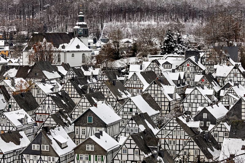 Close-up of snow-covered half-timbered houses and a church in the wintry village in front of the forest, The historic half-timbered houses from the Old Town in Freudenberg