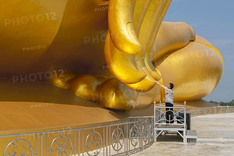 Largest Buddha statue in Thailand (Luang Pho Yai), woman 60-70 touches the fingertips of the statue because according to local belief this brings good luck and success, Wat Muang, Ang Thong, Amphoe Wiset Chai Chan province, Thailand