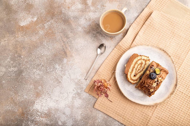 Sweet loaf with cream and caramel, cup of coffee, on brown concrete background with linen beige textile, copy space, top view, flat lay
