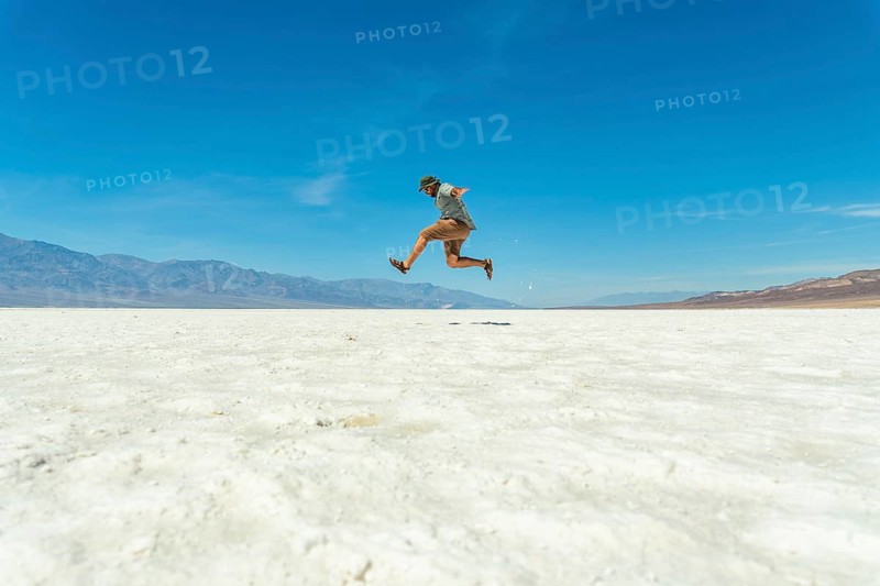 Man jumping joyfully in a vast salt flat landscape under a clear blue sky, experiencing freedom and adventure during a solo trip to death valley national park