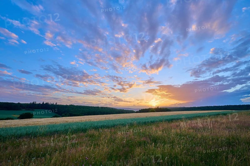 A picturesque sunset spreads over a lush field, the sky is interspersed with warm colors, summer, Großheubach, Miltenberg, Spessart, Bavaria, Germany