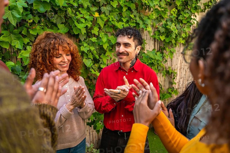Group of diverse individuals participating in a therapy session or support group, clapping hands together, sharing encouragement and feeling connected in a community setting outdoors