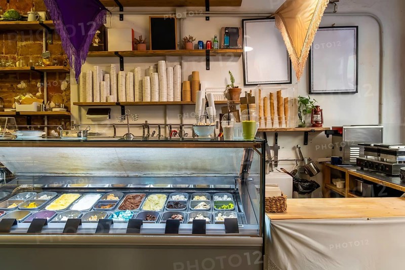 Gelato shop interior with a bright freezer display showcasing colorful artisan ice cream and sorbet flavors, ready for serving in cups and waffle cones to customers
