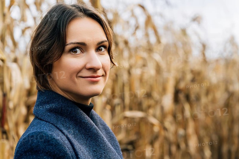 Young woman with short brown hair smiling while standing in autumn in agricultural field