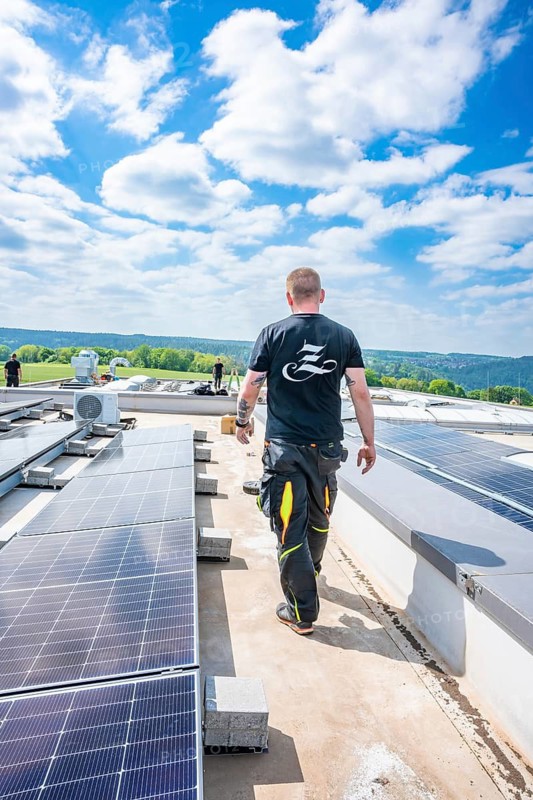 Man walking along solar panels on a roof, blue sky, green nature, PV installation, Perrot company, Calw, Germany