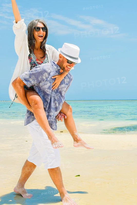 Cheerful young woman playing leapfrog leaning on mans back along turquoise ocean shoreline sandy beach global tropical island resort destination sunny summer day