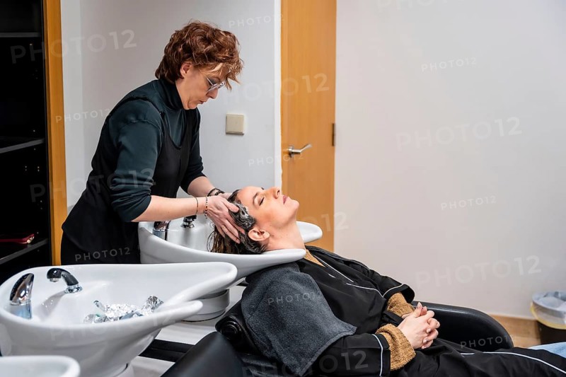 Woman hairdresser shampooing and massaging a reclining female clients hair at a professional salon basin, providing relaxing pampering and care during a beauty treatment