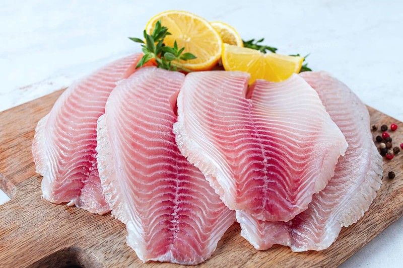 Fresh Tilapia fillet, on a wooden chopping board, with lemon and herbs, ready to cook in the kitchen, no people
