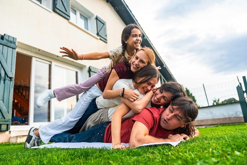 Happy family, including father and four children, enjoying playtime together by building a human pyramid on green grass in the backyard during a summer day